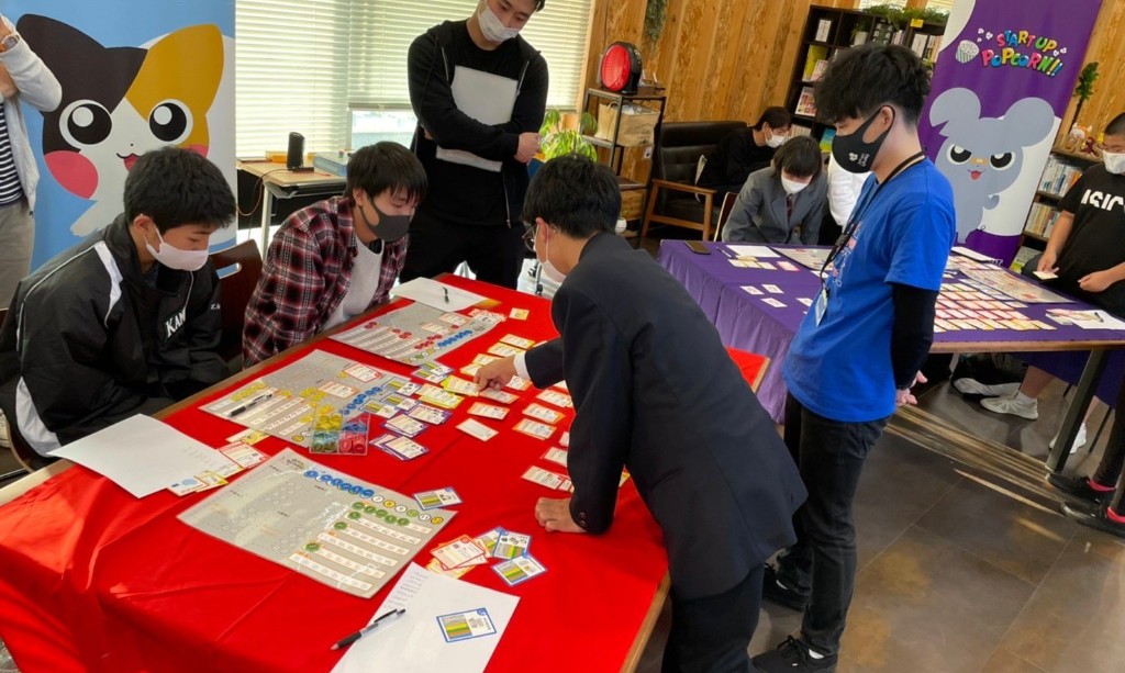 「Investors Try Out!!」のゲームボードとカードを囲み、参加者がシミュレーションに取り組んでいる様子